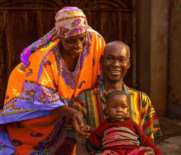 Smiling African family dressed in vibrant traditional clothing, sharing a joyful moment outdoors in Nigeria.